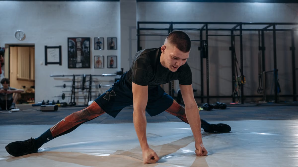 A male athlete stretches intensely in a dimly lit gym environment, preparing for training.